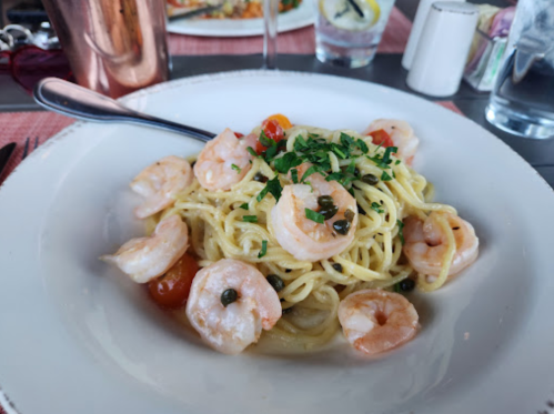 A plate of spaghetti topped with shrimp, cherry tomatoes, and herbs, served with a fork on the side.